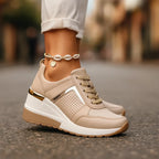 Beige wedge sneakers with gold heel trim and perforated side panel, shown close up with a shell anklet