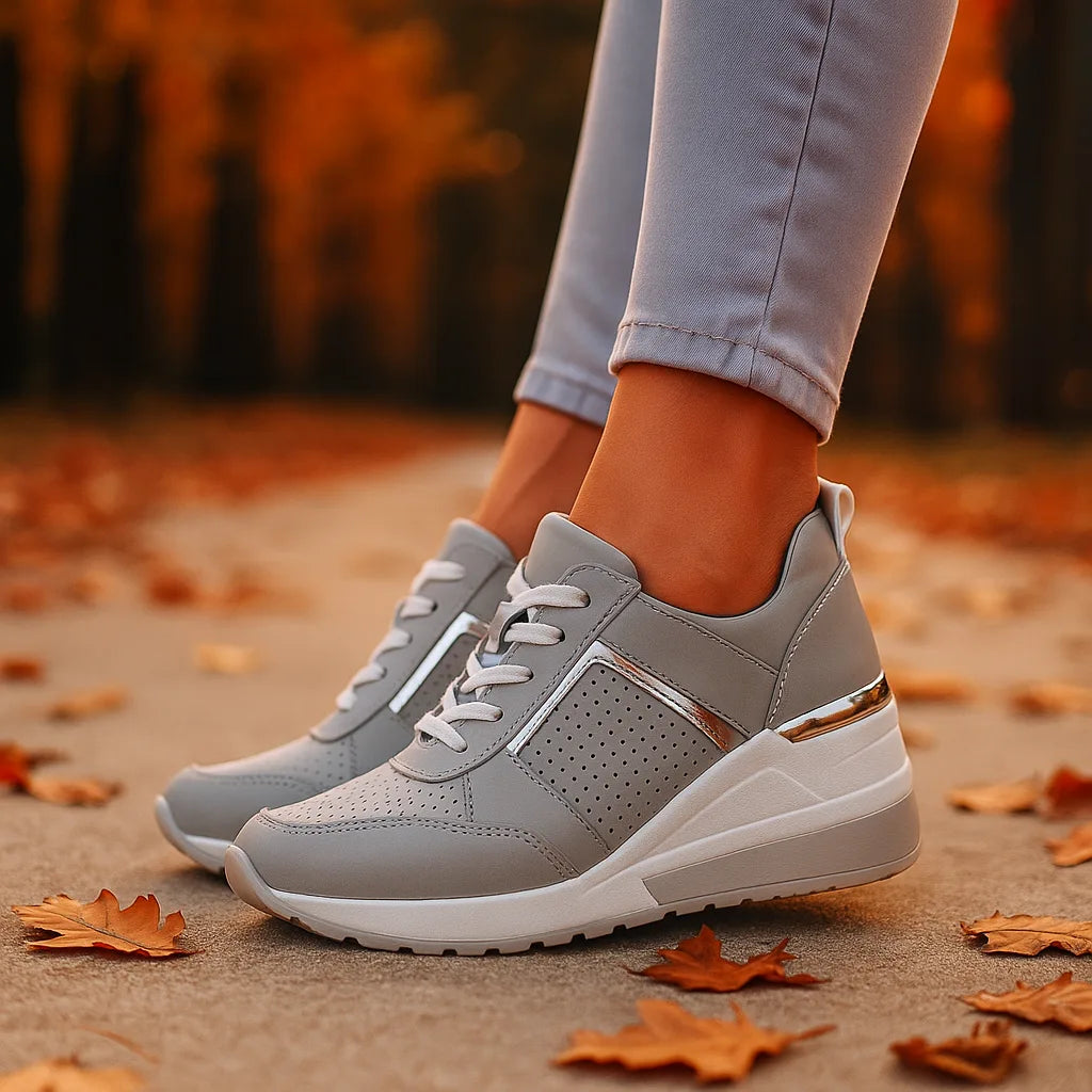 Grey wedge sneakers with silver trim shown from the side, standing among scattered autumn leaves