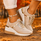 Beige wedge sneakers with gold detailing, heels lifted while walking through fallen autumn leaves
