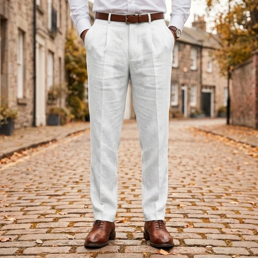 Front view of white pleated linen trousers worn with a brown leather belt and brogue shoes on a cobblestone street