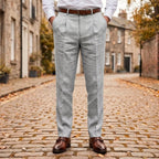 Grey pleated linen trousers styled with a brown belt and monk-strap shoes, front view on cobbled pavement