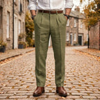 Olive green pleated linen trousers shown with a brown belt and brown Chelsea boots on cobblestones