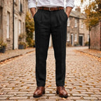 Black pleated linen trousers with cuffed hem, worn with a brown belt and brogue shoes on a cobbled street