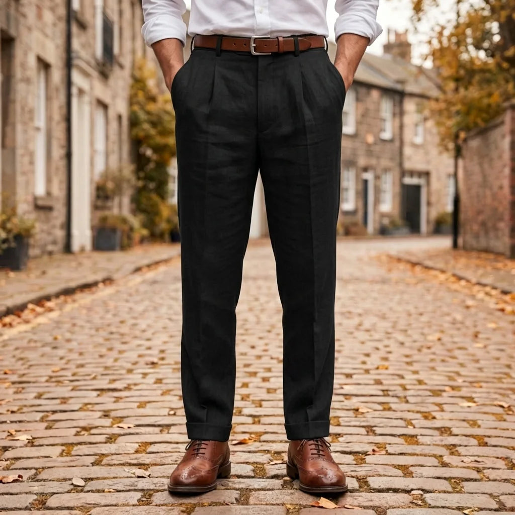 Black pleated linen trousers with cuffed hem, worn with a brown belt and brogue shoes on a cobbled street