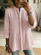 Close-up front view of a pink pintuck-pleated linen shirt with lace trim and button placket, worn with jeans.