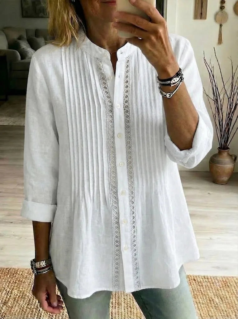 White linen pleated shirt with band collar and lace insert, styled with denim and layered bracelets.
