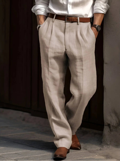 Close-up front view of beige pleated linen trousers worn with a brown leather belt and white shirt