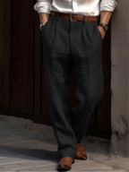 Black pleated linen trousers shown from the front with a brown leather belt and tan shoes