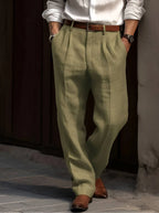 Sage green pleated linen trousers worn with a brown belt, showing the relaxed straight leg