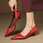 Hand holding one red leather pump by the heel while the other shoe is worn, highlighting the V-cut topline