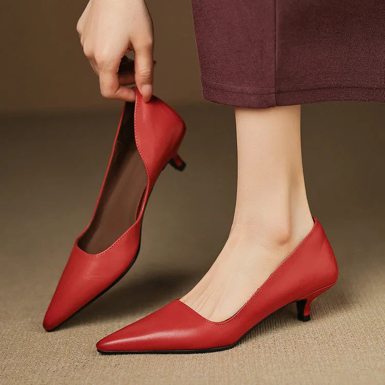 Hand holding one red leather pump by the heel while the other shoe is worn, highlighting the V-cut topline