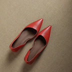 Overhead view of a pair of red pointed-toe flats with a leather insole resting on a woven jute mat