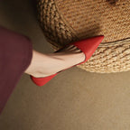 Close-up from above of a red pointed-toe shoe resting against a woven rattan basket