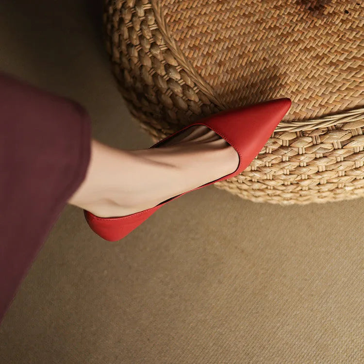 Close-up from above of a red pointed-toe shoe resting against a woven rattan basket