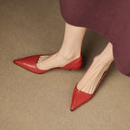 Top-down view of two feet wearing red pointed-toe heels crossed over each other on a jute rug