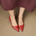 Front view of both feet in red pointed kitten heels peeking out from under a maroon dress