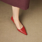 Close-up top-down view of one red pointed-toe shoe on a woven textured surface