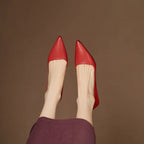 Close-up side profile of a red pointed-toe shoe with low heel on a jute mat under a maroon hemline