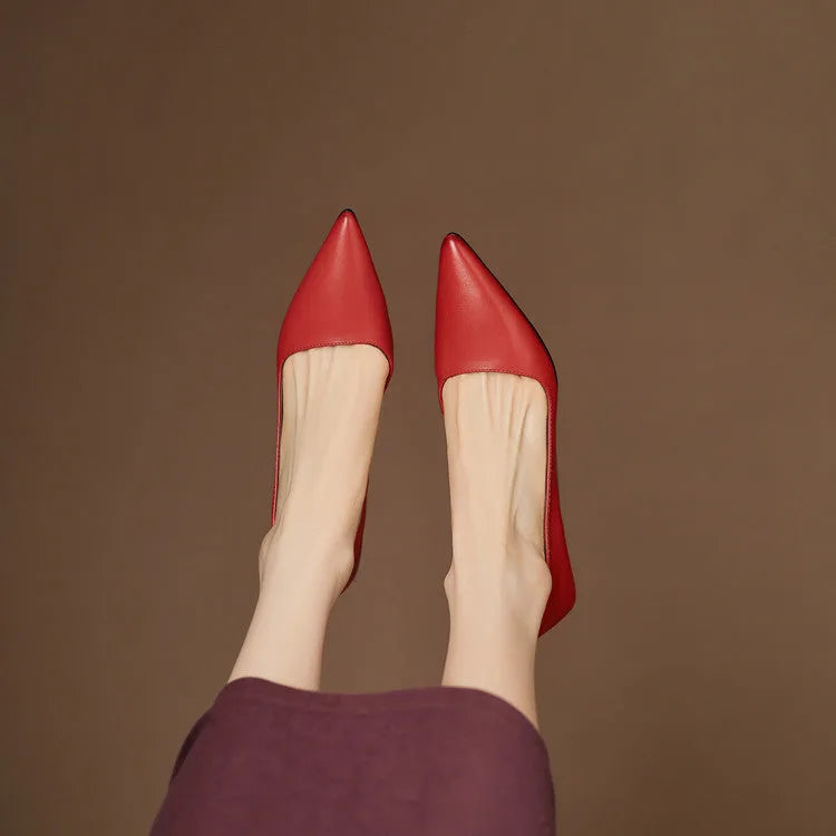 Close-up side profile of a red pointed-toe shoe with low heel on a jute mat under a maroon hemline