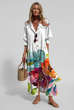 Woman wearing a white printed linen maxi shirt dress with teal and orange watercolour floral print, holding a woven bag