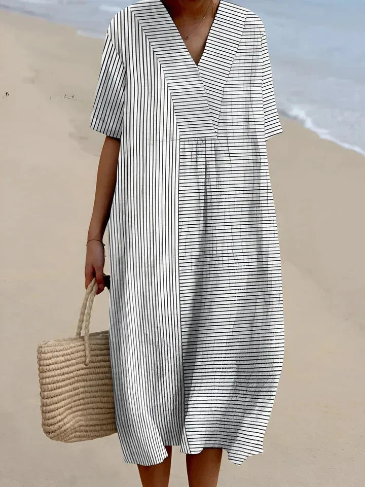 Monochrome striped V-neck midi dress with short sleeves, paired with a straw tote, model walking on sand