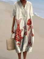 Pale grey V-neck midi dress featuring a bold red and gold fish print across the front, worn with a woven tote bag