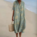 Sage green V-neck midi dress with an allover cream floral print, short sleeves and relaxed silhouette, shown beachside