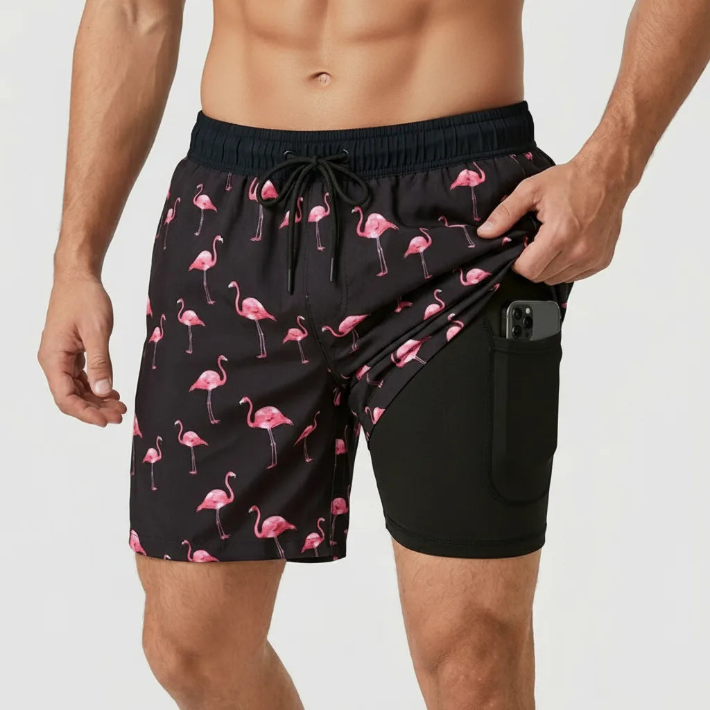 Front view of black swim shorts with pink flamingo print, pocket pulled open to reveal black compression liner with phone pocket