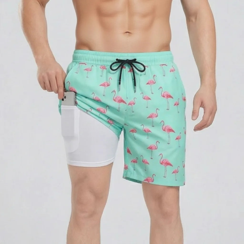 Front view of mint green swim shorts with pink flamingo print, side pocket open showing white compression liner holding a phone