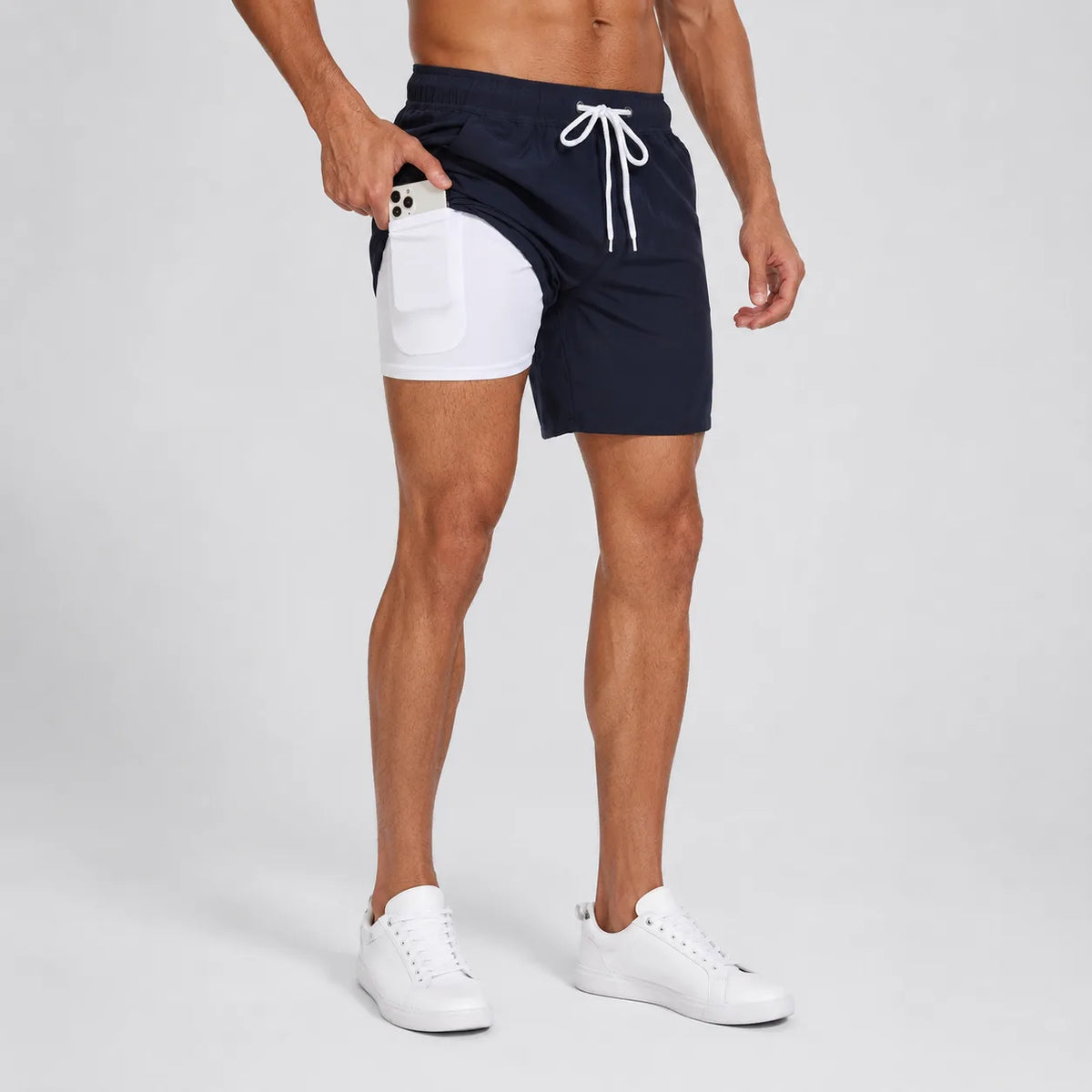 Side view of man wearing navy swim shorts with white compression liner, pulling a phone from the inner pocket