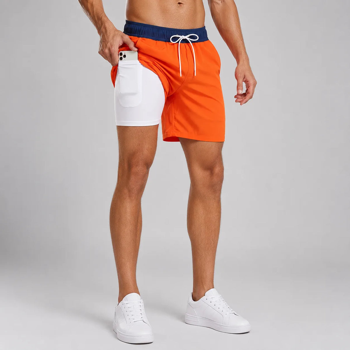 Man in orange and navy colour-block swim shorts with white compression liner, phone tucked in side pocket