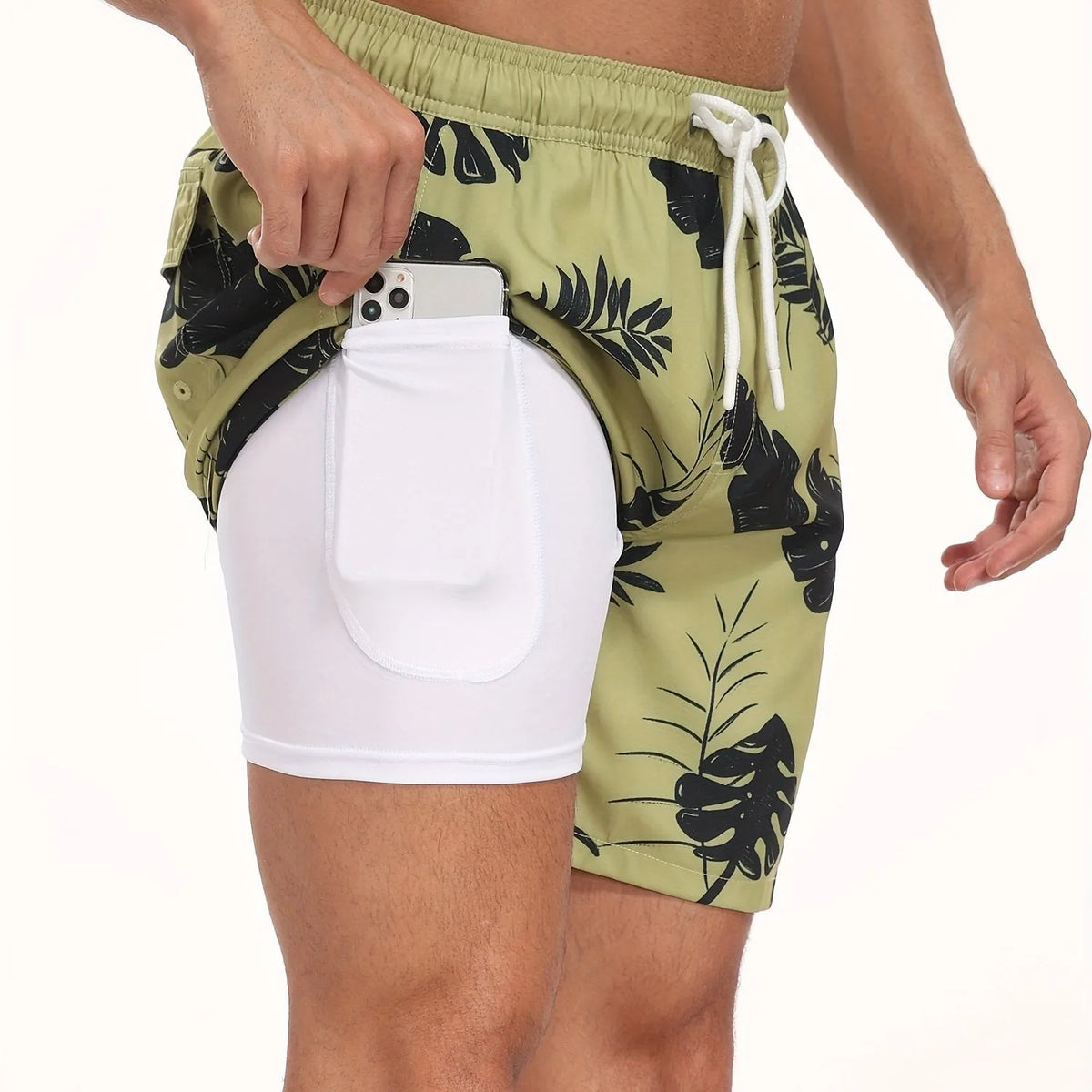 Close-up of green palm leaf print swim shorts showing white compression liner and inner pocket with phone