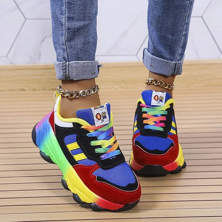 Blue and red chunky sneakers with rainbow laces and gel sole, worn with cuffed jeans and gold anklets