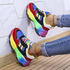 Blue and red chunky trainers shown from the side against a tiled wall, rainbow laces and gel heel visible
