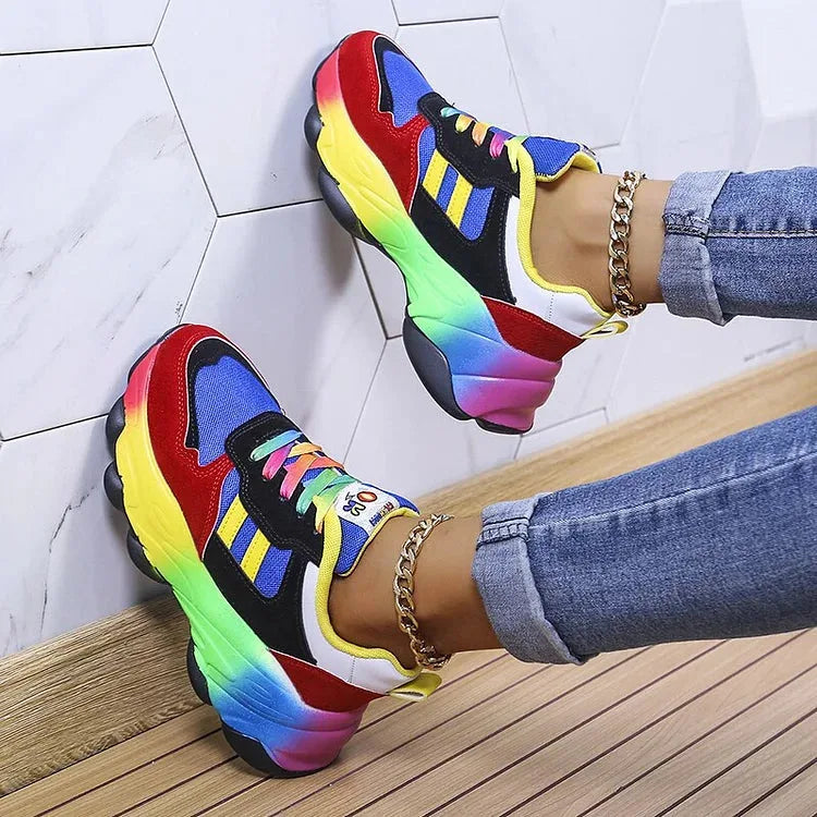 Blue and red chunky trainers shown from the side against a tiled wall, rainbow laces and gel heel visible