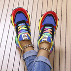 Top down view of blue and red chunky sneakers with multicoloured laces, worn with ankle chain jewellery