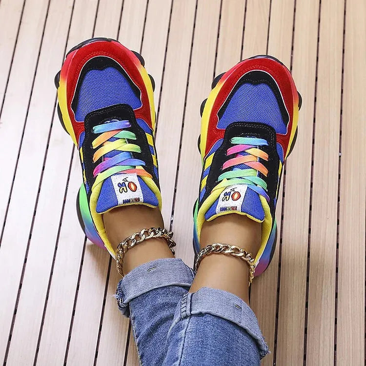 Top down view of blue and red chunky sneakers with multicoloured laces, worn with ankle chain jewellery