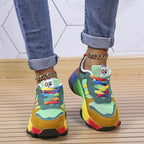 Rear angle of green and mustard sneakers on wooden decking, showing padded collar and rainbow sole stripes