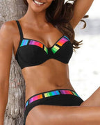 Close-up of black underwire bikini top with rainbow stripe panel detail and matching high-waisted bottoms against a palm tree