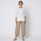 Woman wearing a white long-sleeve top with relaxed tan linen-blend pants and knit sandals, full-length front view