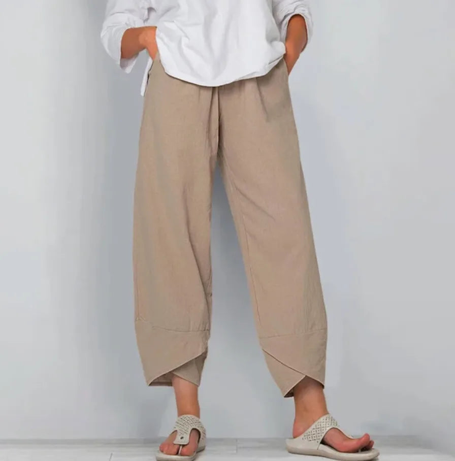Close-up front view of tan linen-blend pants with elastic waistband and curved tulip hem, worn with sandals