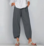 Front view of grey linen-blend pants with relaxed wide leg and curved hem, worn with a white top