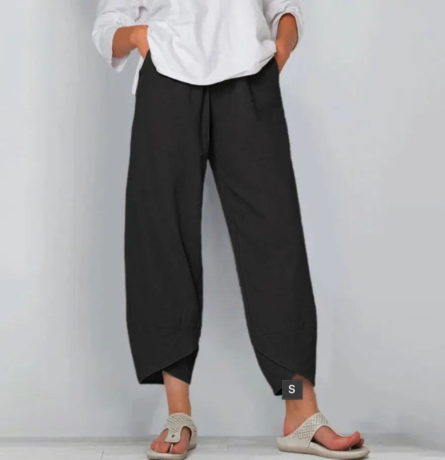 Front view of black linen-blend pants with relaxed wide leg and tulip hem, paired with knit sandals