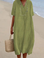 Light green V-neck midi dress with relaxed wrap front and short sleeves, styled with a straw tote bag