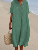 Sage green crinkled midi dress with notched V-neck and button accents, paired with a woven beach bag