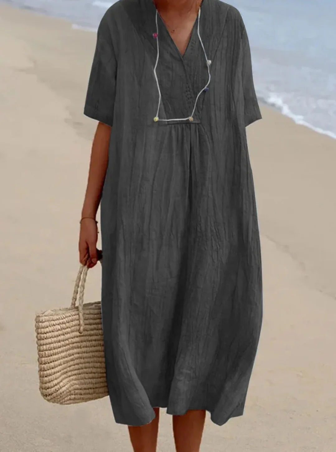 Dark grey relaxed-fit V-neck midi dress with textured crinkle fabric and short sleeves on the sand