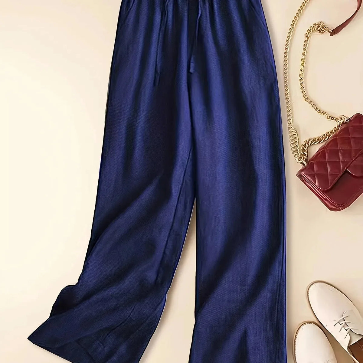 Styled flat lay of linen pants with a quilted red crossbody bag, gold chain strap and white sneakers