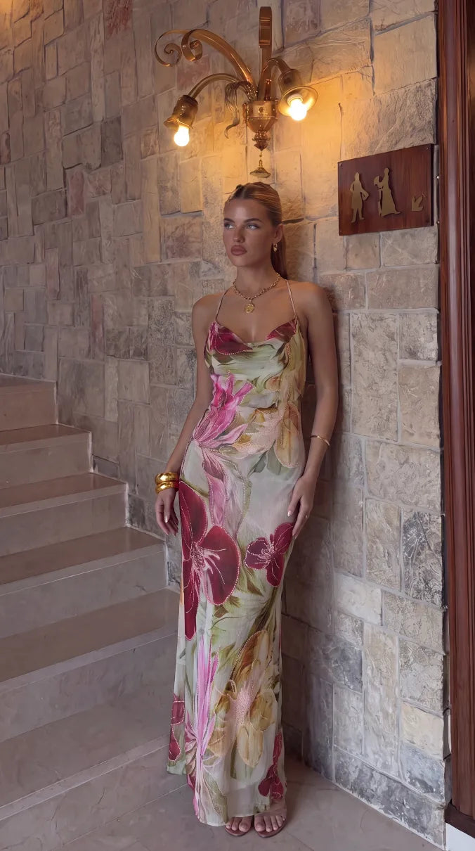 Full front view of the beaded floral maxi dress leaning against a stone wall, paired with gold jewellery and heeled sandals