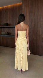 Rear view of pale yellow pleated maxi dress showing halter tie closure and ruffle cascading down the back