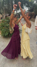 Two women dancing outdoors in plum and yellow pleated ruffle maxi dresses with matching accessories